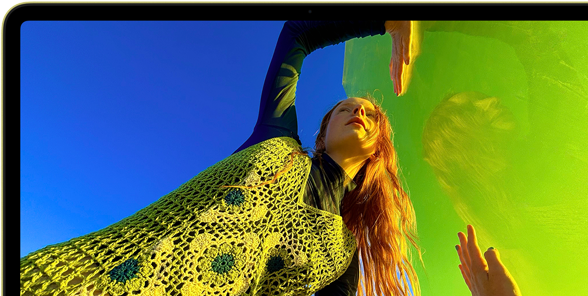 جهاز MacBook Neo، لون أصفر سيتروس، شاشة تعرض شخصاً مبتسماً يستلقي في حقل أزهار مشمس