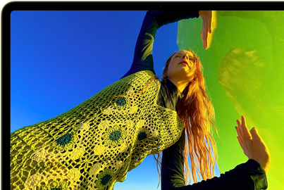 جهاز MacBook Neo، لون أصفر سيتروس، شاشة تعرض شخصاً مبتسماً يستلقي في حقل أزهار مشمس