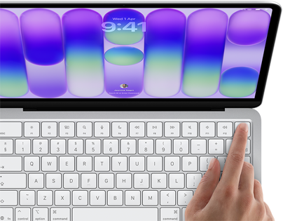 MacBook Neo, silver color, showing login screen, person's finger on Touch ID sensor in top-right corner of keyboard