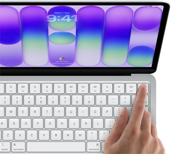MacBook Neo, silver color, showing login screen, person's finger on Touch ID sensor in top-right corner of keyboard